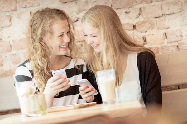 To unge jenter som ler og ser på mobil. Foto